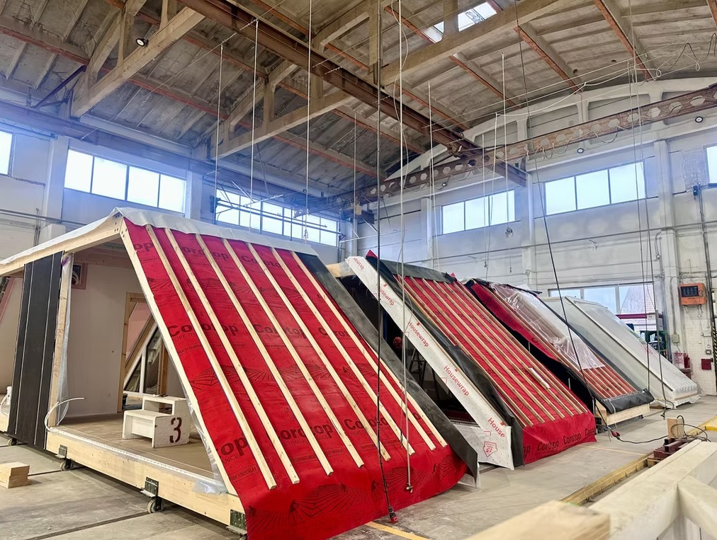 Home modules with weather-wrapped pitched roofs lined up inside the factory